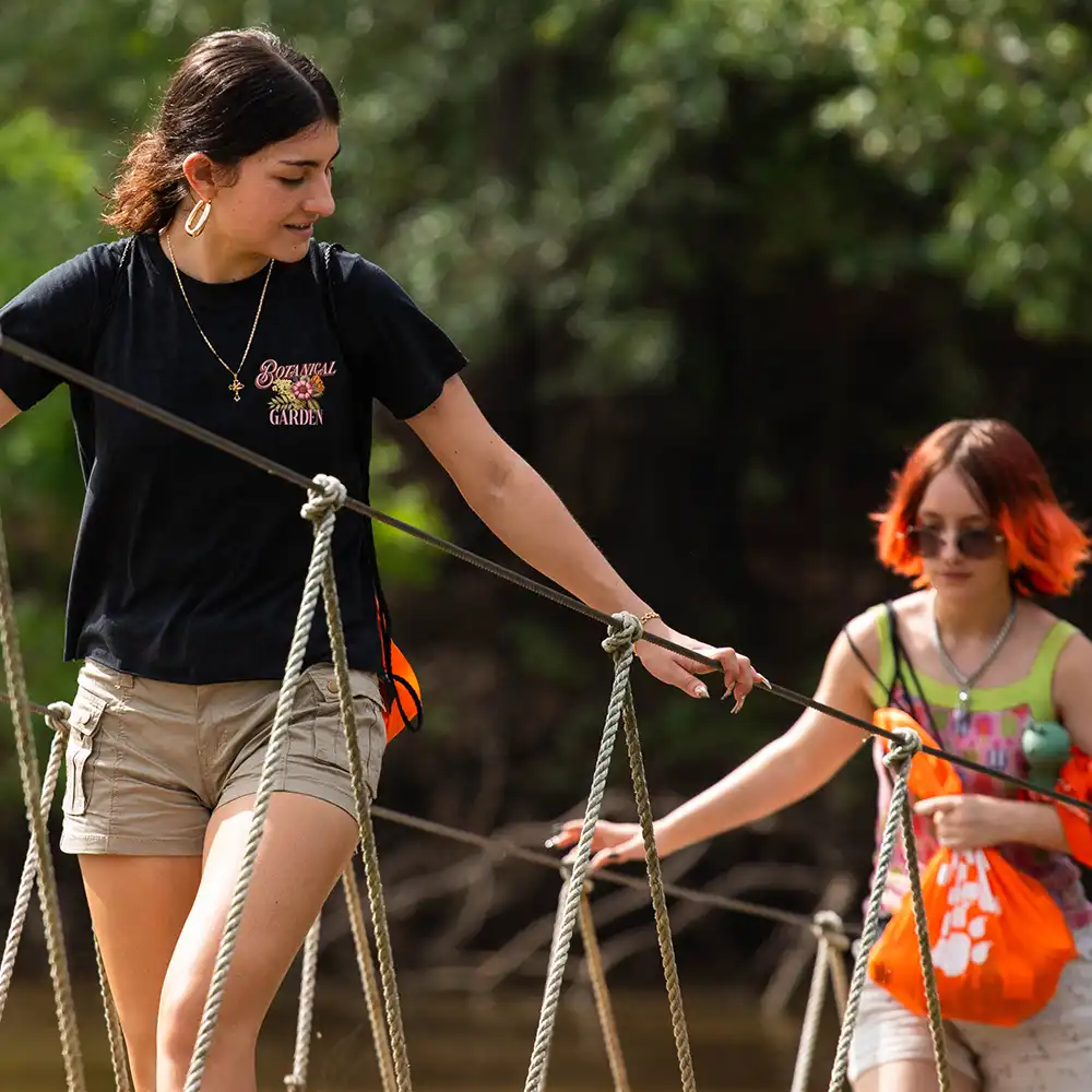 Two girls walking across an outdoor bridge. 